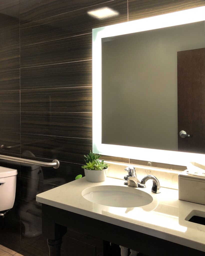 Restroom featuring backlit mirror and dark tile wall, designed with luxury medical spa interior design aesthetics.