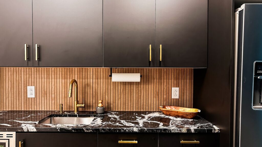 Kitchenette area featuring black marble countertop, gold faucet, and vertical wood backsplash.