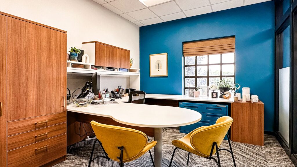 Executive office with wood cabinets, round table, and yellow upholstered chairs.