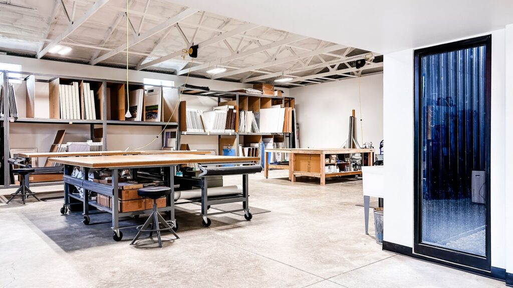 Workshop space with large cutting tables and shelving for framing materials.