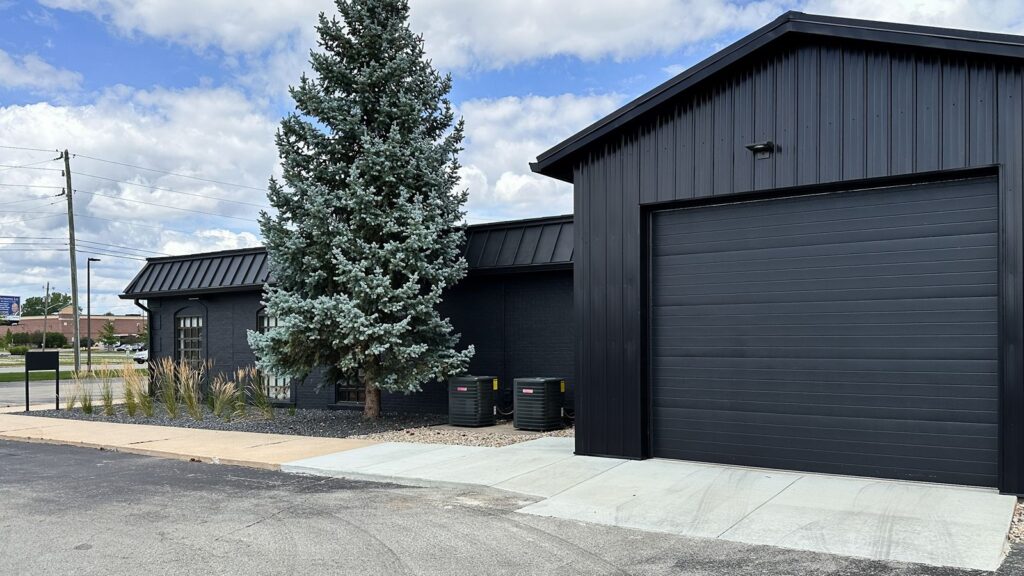 Side exterior of renovated studio with updated black metal roof and entryway.