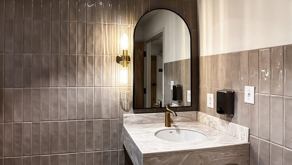 Restroom with tile accent wall, arched mirror, and brass fixtures in modern dental office.