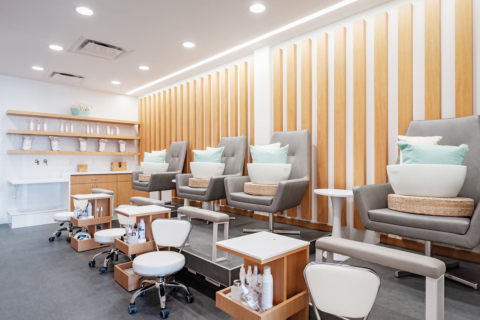 Nail salon pedicure area with modern spa chairs and wood accent wall.