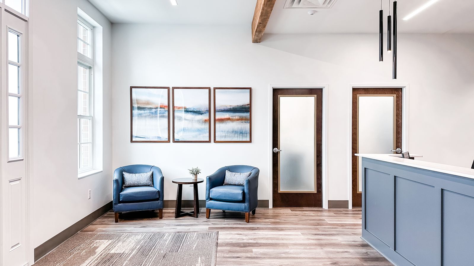 Modern waiting area at Stonegate Complex in Zionsville, Indiana, featuring two blue chairs, abstract art, and a blue reception desk in a bright room—ideal for corporate financial planning clients.