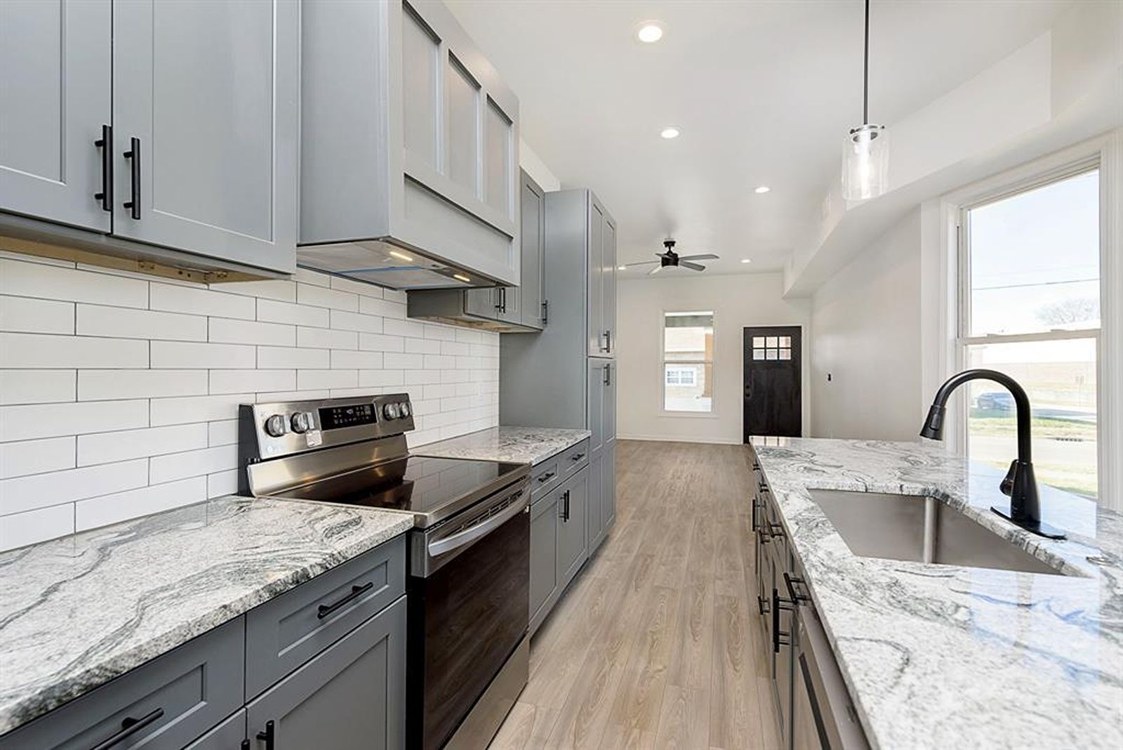 Modern kitchen remodel with gray cabinets and marble countertops.