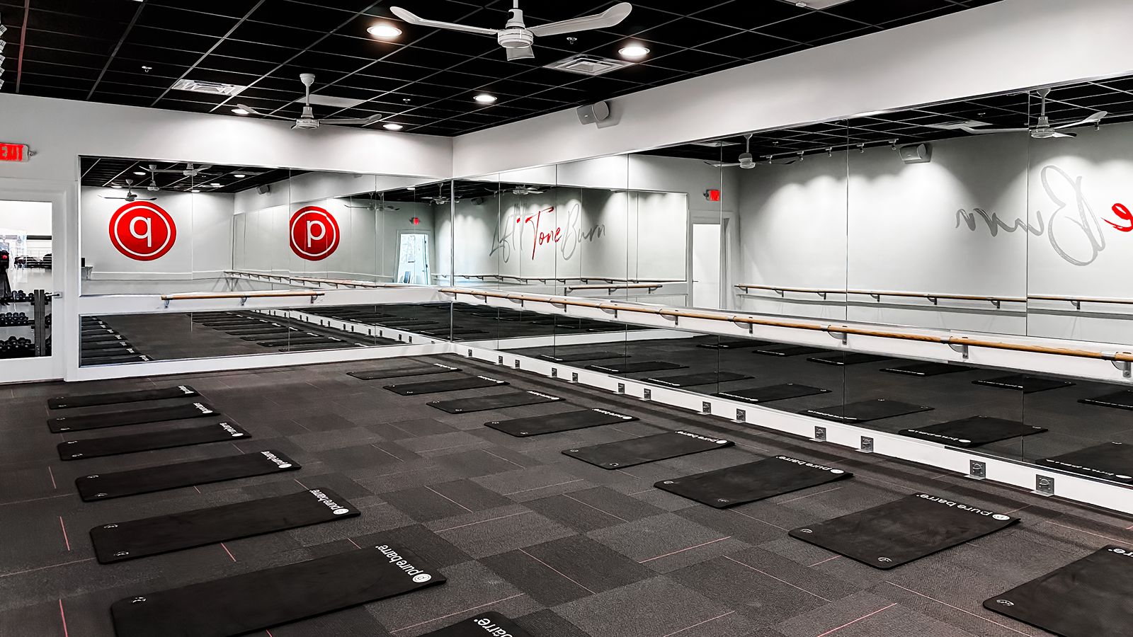 Barre fitness studio interior with mirrored walls and black mats arranged on the floor.