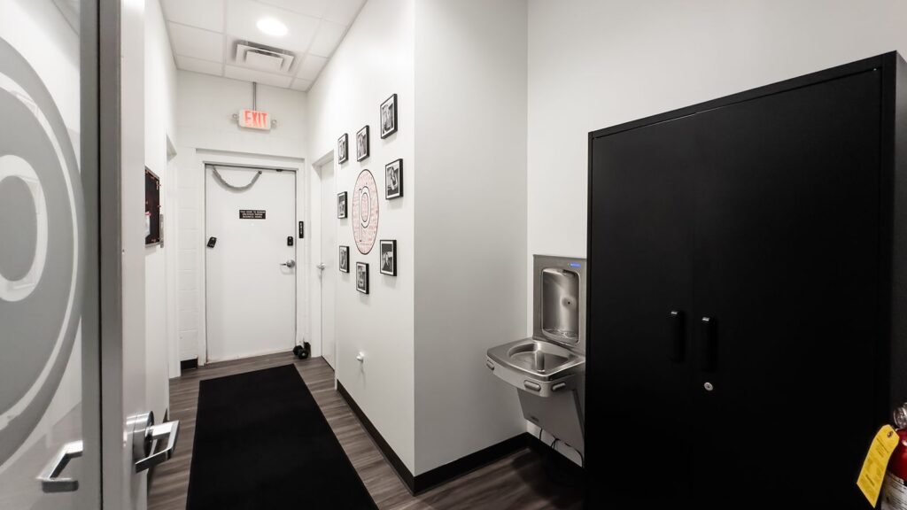 Hallway with black flooring and framed photos leading to studio entrance.