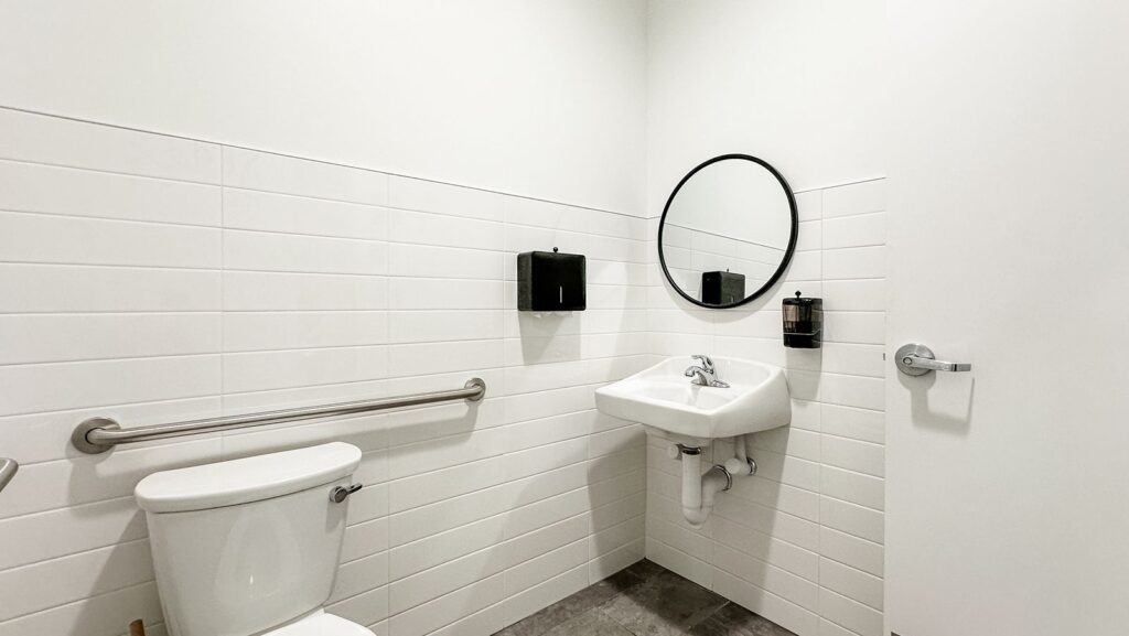Accessible restroom with modern white tile and circular mirror.