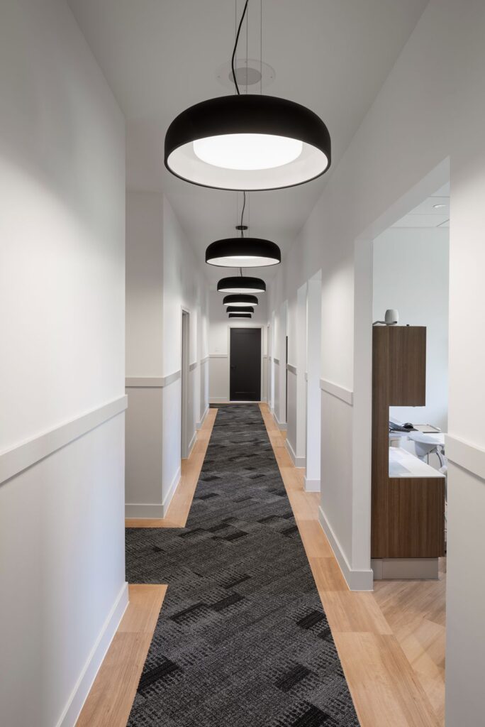 Bright clinical hallway leading to dental operatories with modern ceiling lighting.