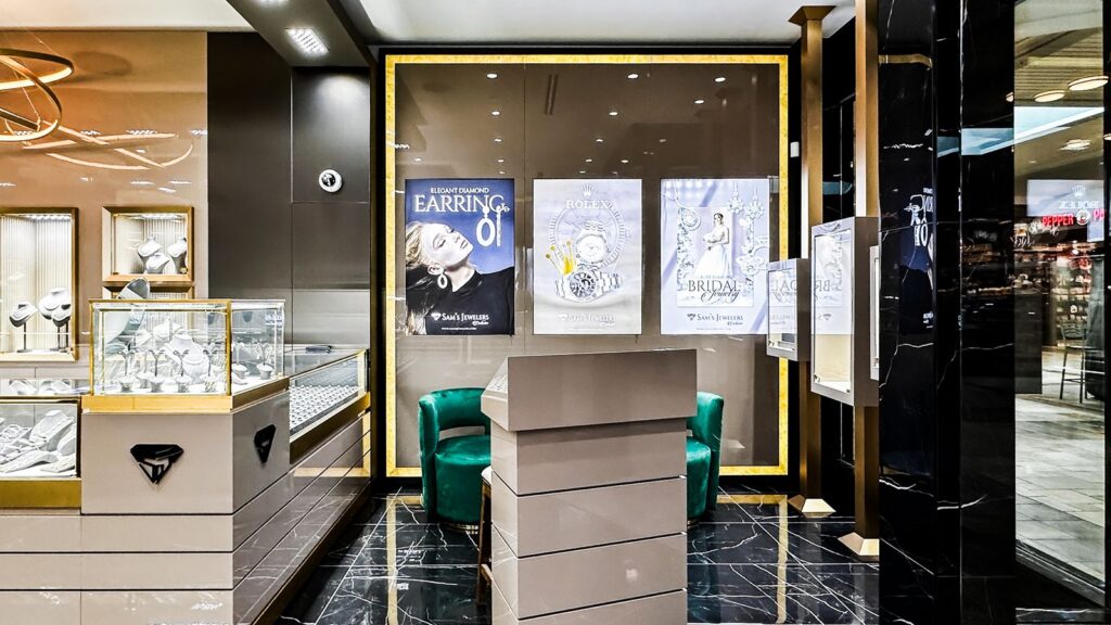 Seating area with green velvet chairs beside framed jewelry artwork.