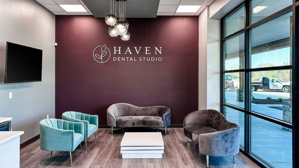 Lobby seating area with velvet chairs and branded wall for Haven Dental Studio.