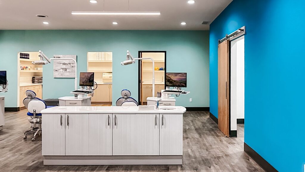 Consultation room with dental chair, dual monitors, and white walls.