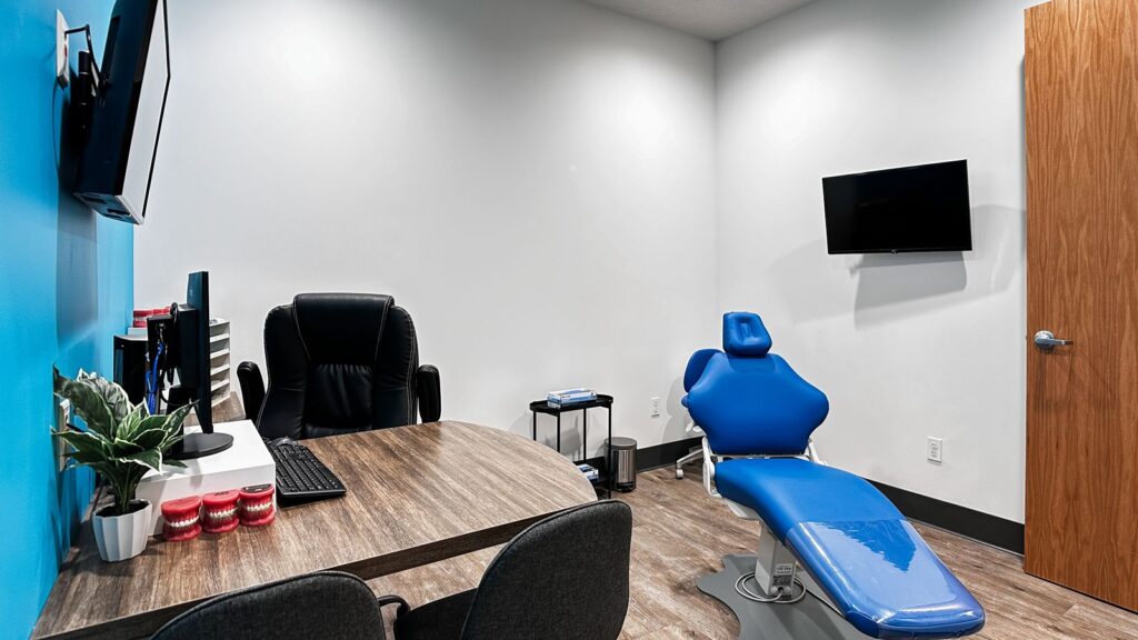 Consultation room with dental chair, flat screen monitor, and blue accent wall.