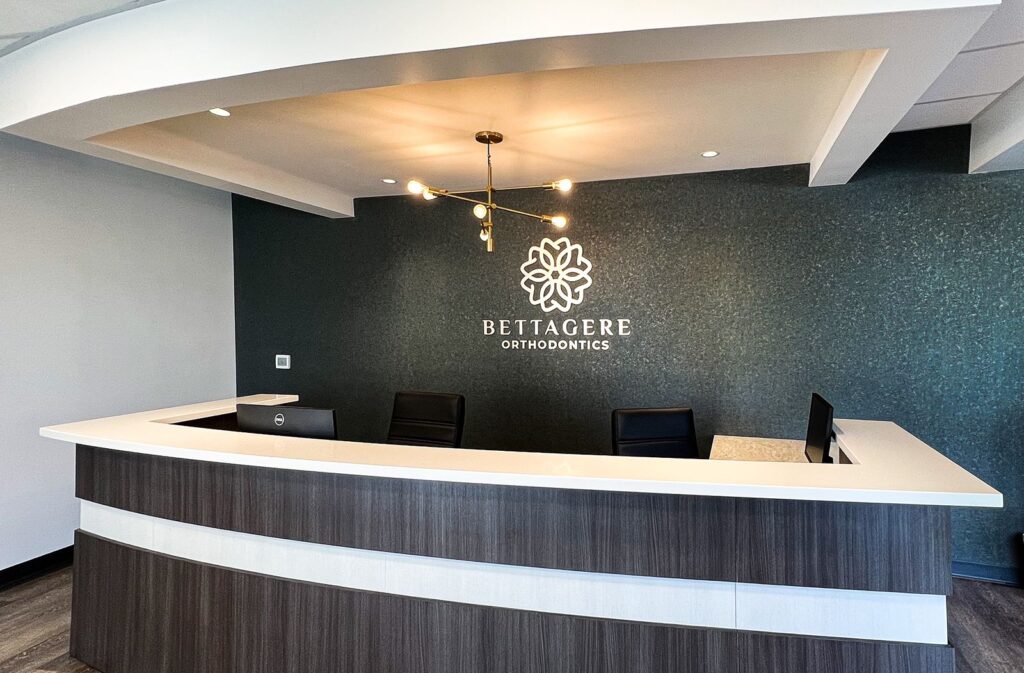 Reception area of Bettagere Orthodontics featuring custom desk and textured wall design by commercial interior design firms.