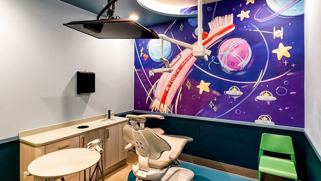 Whimsical hallway with forest-inspired murals and train-track flooring designed by dental office architects.