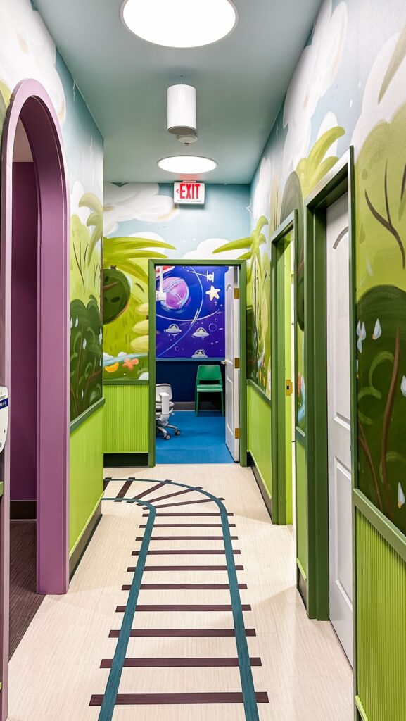 Hallway leading to pediatric exam rooms featuring murals, arches, and wellness-focused dental design.