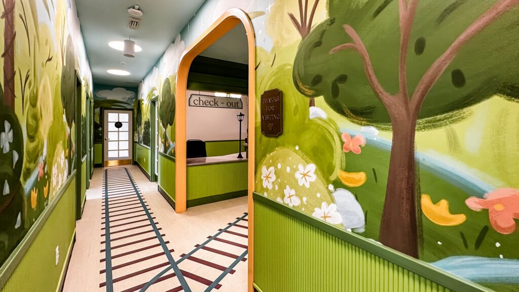 Hallway with train-track flooring and colorful murals reflecting imaginative pediatric dental clinic interior design.
