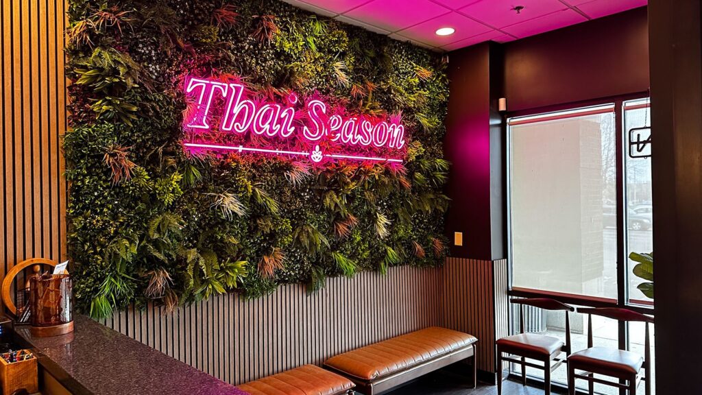 Entry lounge area with pink neon signage, living wall greenery, and wood accents.