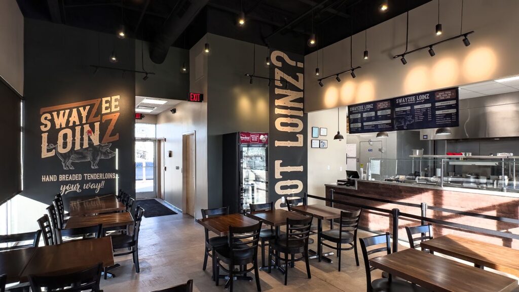 Dining area with dark wood tables and branded wall graphics for Swayzee Loinz.