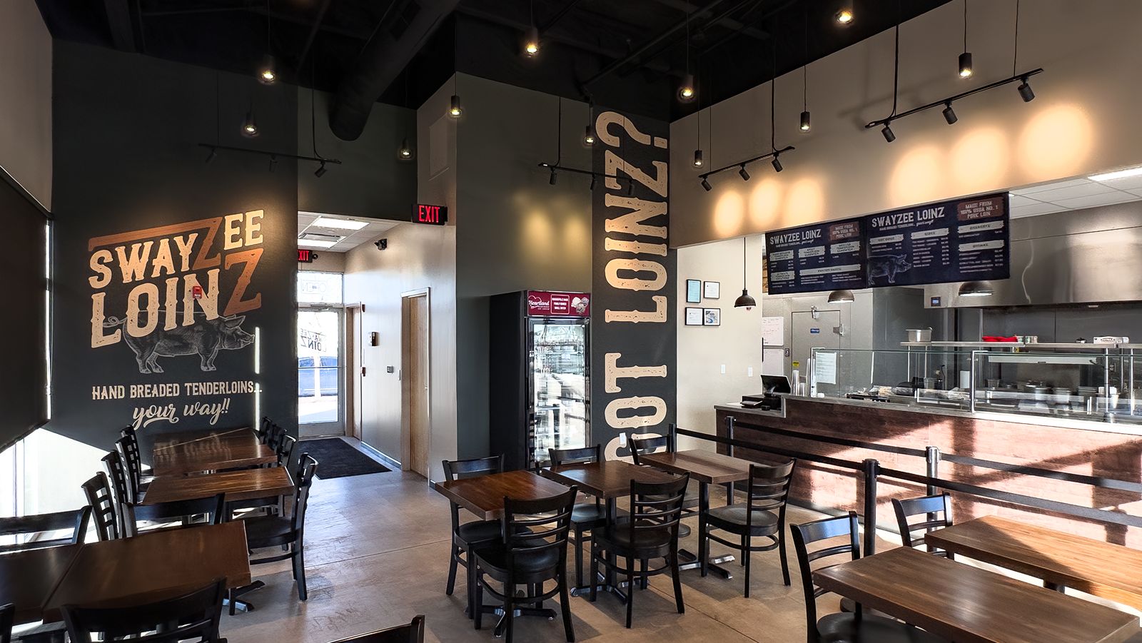 Dining area with dark wood tables and branded wall graphics for Swayzee Loinz.