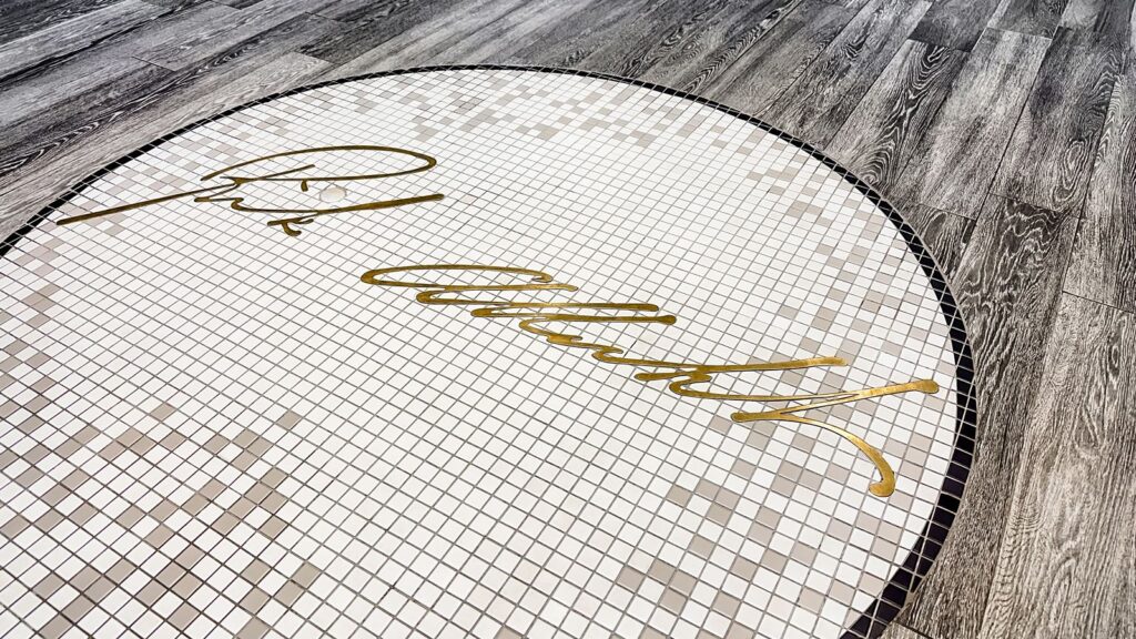 White mosaic tile floor inlay with gold Rick’s Cafe Boatyard signature.