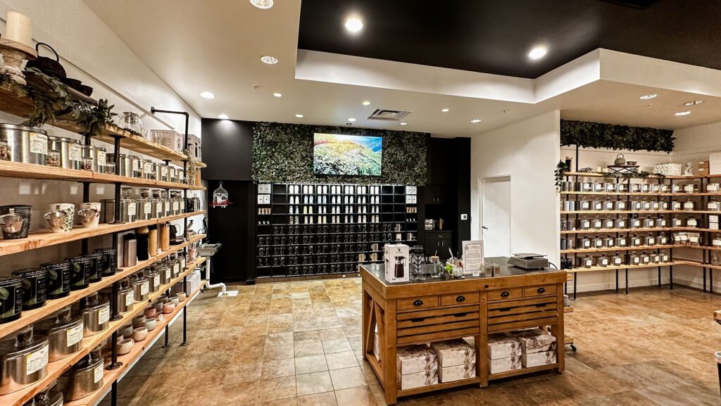 Wall of tea tins under accent lighting with greenery decor.